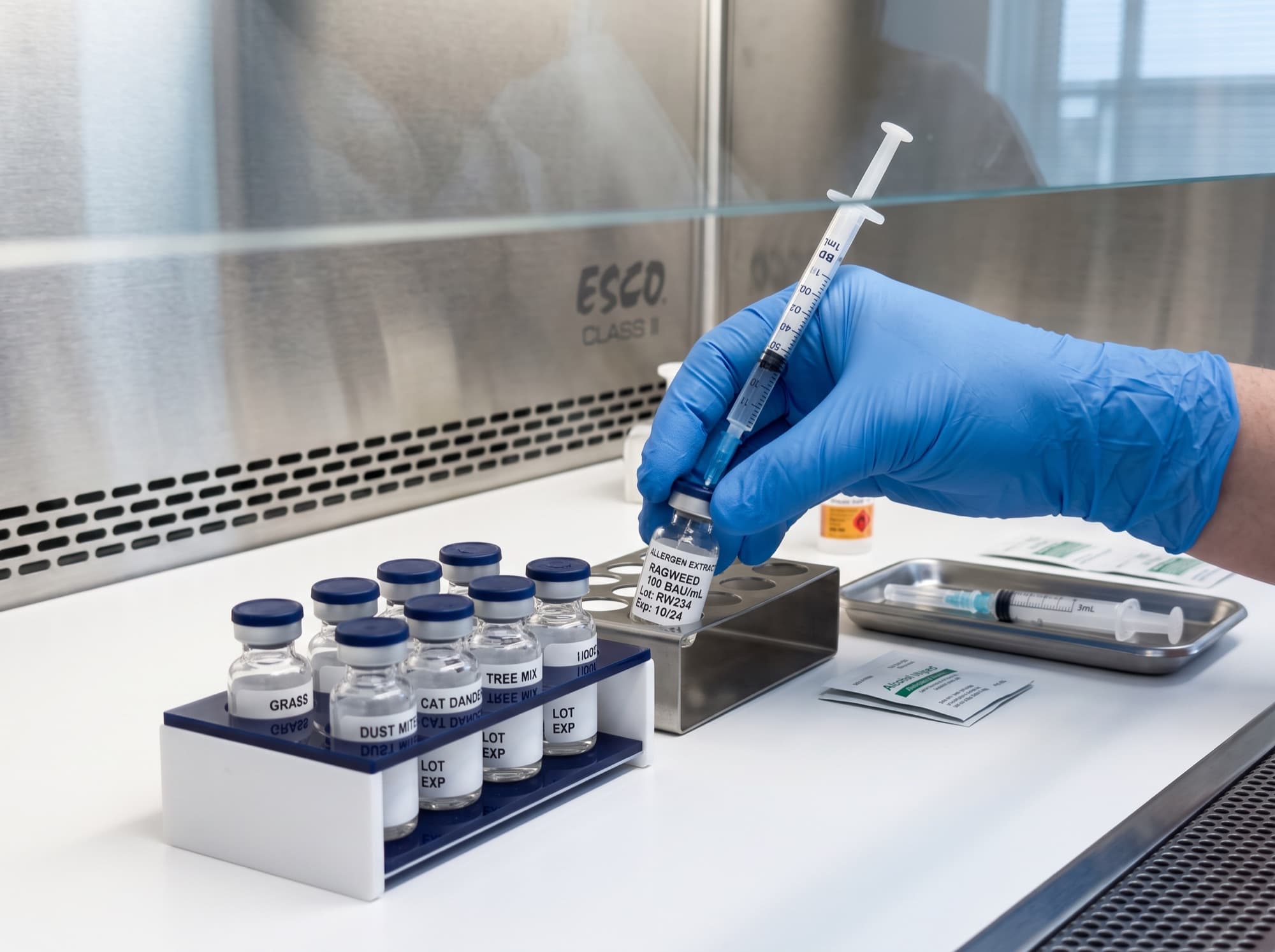 Allergen immunotherapy vials and a syringe prepared by a gloved pharmacist under a laminar-flow hood.